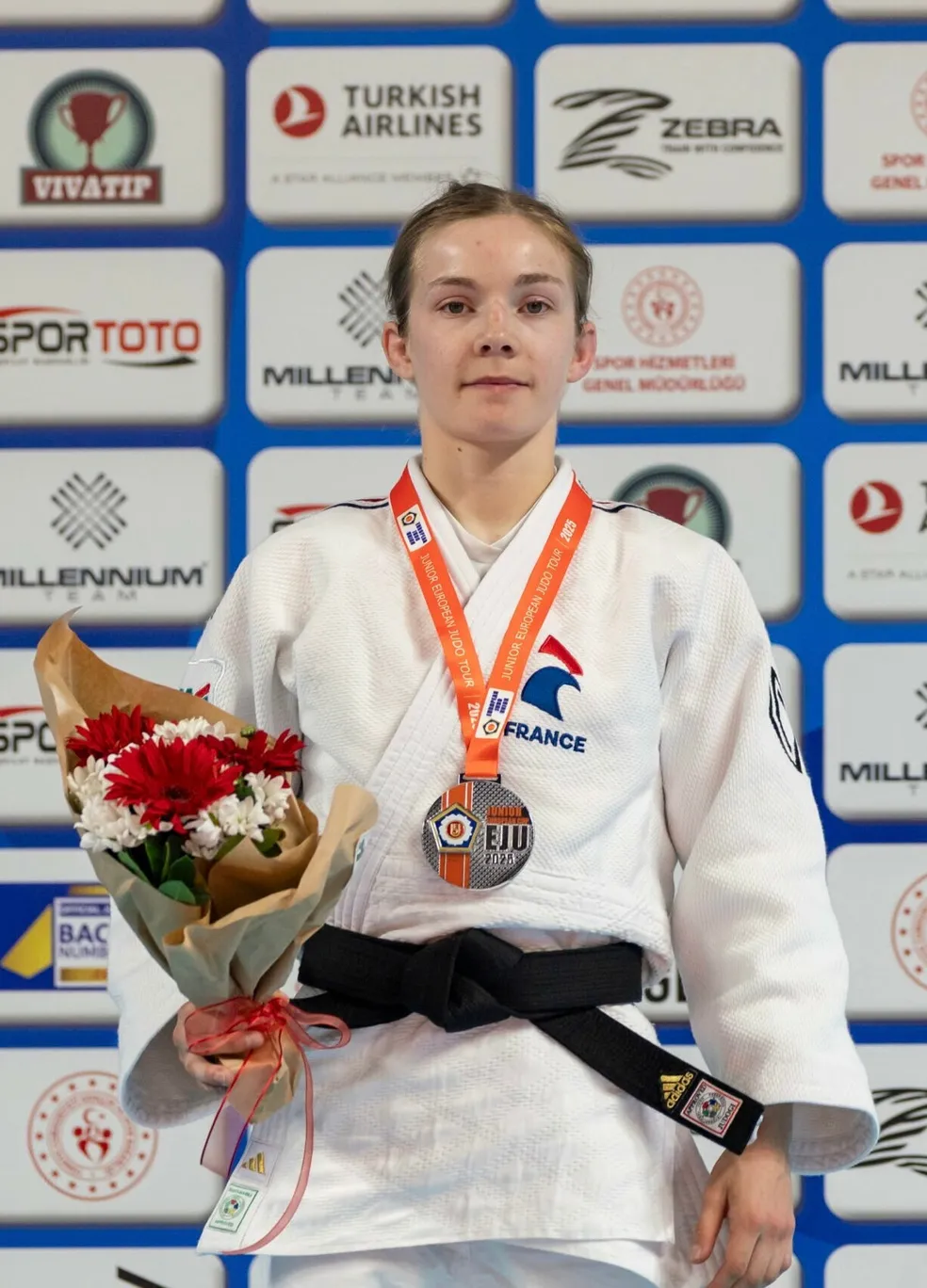 Clara Mermet en kimono blanc, médaille autour du cou et bouquet de fleurs à la main